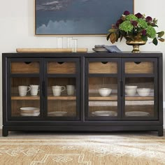 a black cabinet with glass doors and plates on it in front of a vase filled with flowers