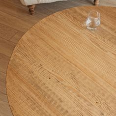 an empty glass sits on top of a round wooden table in a room with hardwood floors