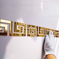 a person in white gloves is touching the letters on a wall with gold foiling