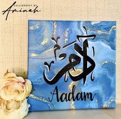 an islamic calligraphy is displayed on a table next to some flowers and a vase