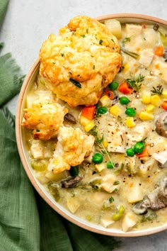 a bowl filled with chicken pot pie soup next to a muffin on top of a green napkin