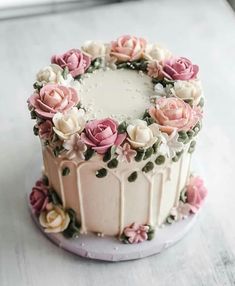 a cake decorated with pink and white flowers on a plate, sitting on a table