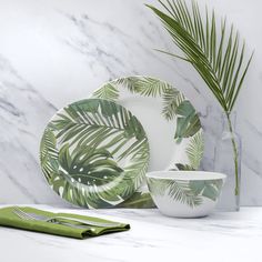 a plate, bowl and napkin on a marble countertop with a palm leaf print