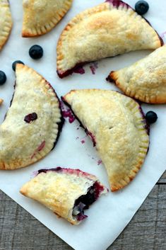 blueberry hand pies are arranged on a piece of parchment paper with fresh blueberries in the middle