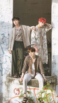 three young men sitting on the ledge of an old building with graffiti all over them