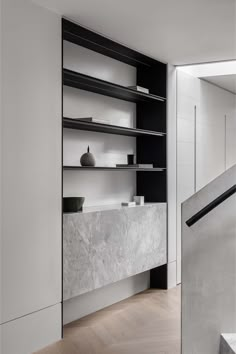 a white and black room with stairs, shelves and vases on the wall next to it