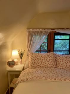 a bed with white sheets and pillows in a bedroom next to a window that looks out onto the woods