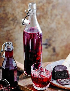 a bottle of red wine next to two glasses with ice and cookies on the side