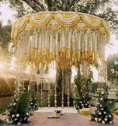 an outdoor wedding setup with white flowers and gold chains hanging from the ceiling, surrounded by greenery