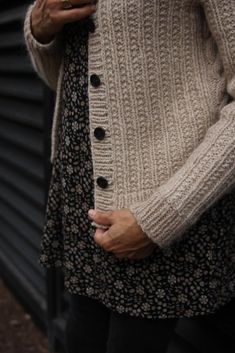 a woman is holding her cell phone and wearing a cardigan sweater while standing in front of a building