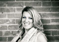 a black and white photo of a smiling woman in front of a brick wall with blue eyes