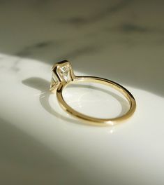 a yellow gold engagement ring with a single diamond on it's side, sitting on a white surface