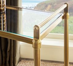 a glass and brass table in front of a window with a view of the ocean