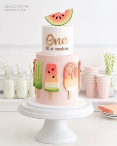 a pink cake with popsicles and watermelon slices on the top is surrounded by other desserts