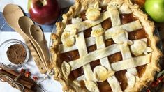 an apple pie on a table with apples and cinnamon sticks