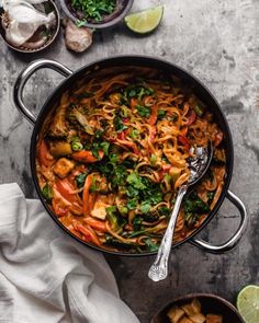 a pan filled with noodles and vegetables next to some lime wedges on the side