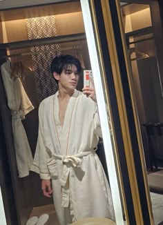 a man in a bathrobe taking a selfie with his cell phone while standing in front of a mirror