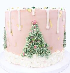 a pink and white christmas cake with icing on it's top, decorated with a tree