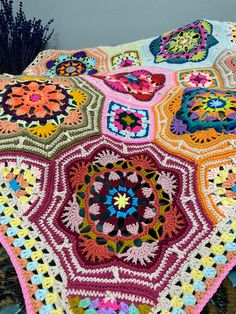 a colorful crocheted blanket on top of a wooden table next to purple flowers