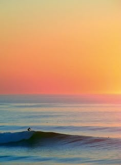 a person riding a wave on top of a surfboard in the ocean at sunset