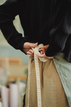 a person wearing a brown apron and holding a white ribbon around their waist with both hands