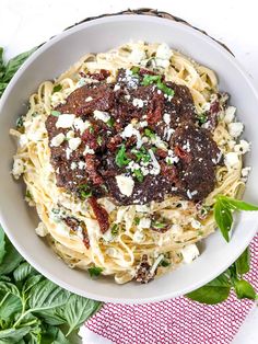 a white bowl filled with pasta covered in meat and cheese on top of green leaves