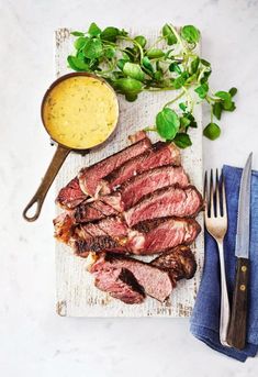 steak with mustard sauce and fresh herbs on cutting board next to knife, fork and spoon