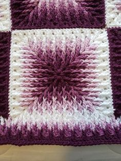 a purple and white crocheted blanket sitting on top of a bed