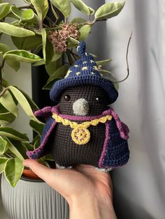 a hand holding a small crocheted stuffed animal in front of a potted plant