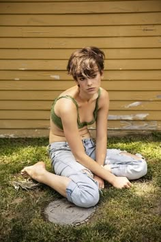 a young woman sitting on the ground in front of a house with her legs crossed