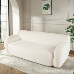 a white couch sitting on top of a wooden floor next to a potted plant