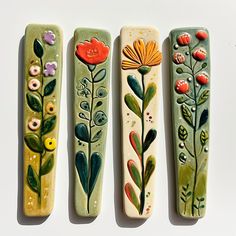 three ceramic book ends decorated with flowers and leaves, one painted in yellow, the other green