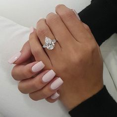 a woman's hand with pink manicured nails holding a diamond ring