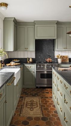 a kitchen with green cabinets and black counter tops, gold trimming on the backsplash