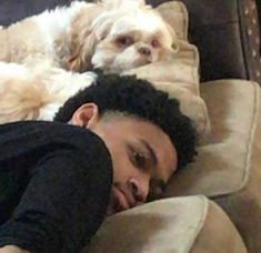 a man laying on top of a couch next to a dog with his head resting on the pillow