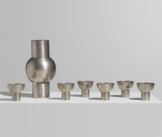 a group of silver cups and vases sitting on a white table with grey background