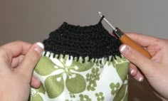 two hands holding a crocheted purse with a needle in it and another person's hand working on the fabric