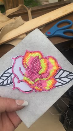 a hand holding a piece of fabric with a flower on it and scissors in the background