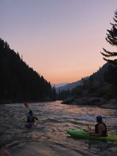 two people in kayaks paddling down a river at sunset with mountains in the background