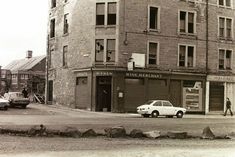 an old black and white photo of a car parked in front of a building