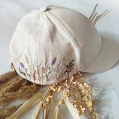 a white hat with flowers on it sitting next to dried grass