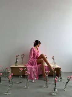 a woman in a pink dress sitting on a bench surrounded by vases and flowers