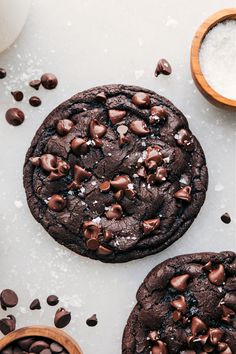 two cookies with chocolate chips and sea salt next to them on a white counter top