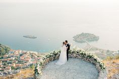 a bride and groom standing on top of a hill overlooking the ocean with an island in the background