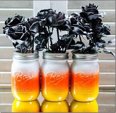 three mason jars with flowers in them are sitting on a counter top, one is painted yellow and the other has black roses