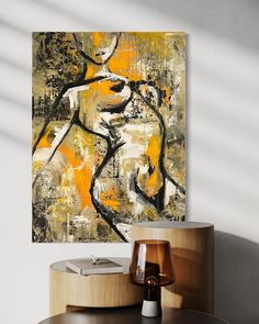 an abstract painting hangs on the wall above a round table with a lamp and vase