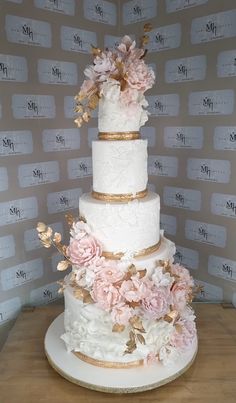 a three tiered wedding cake with pink flowers on the top and gold trimmings