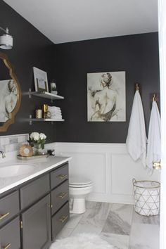 a bathroom with gray cabinets and white towels on the rack above the toilet is decorated with gold accents