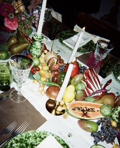 a table topped with lots of different types of fruits and veggies next to candles