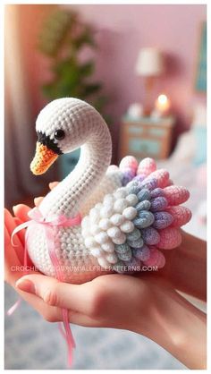 a crocheted swan sitting on top of a person's hand in front of a bed